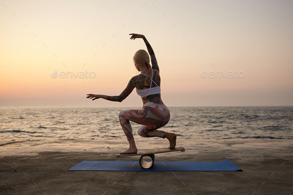 Pretty young healthy woman with casual hairstyle holding pose on balance board on seafront