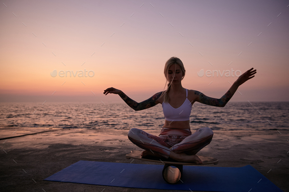 Young healthy blonde woman in good physical condition sitting on balance board with crossed legs