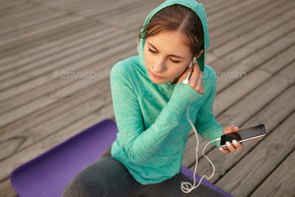 Photo of cute girl in bright sportswear, listening cool playlist on headphones after morning yoga