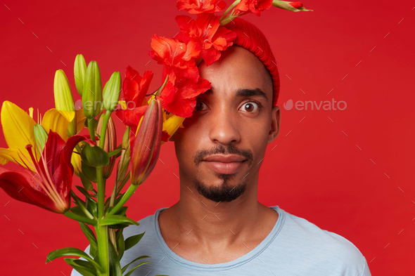 Young shocked attractive guy in red hat and blue t-shirt, holds a bouquet