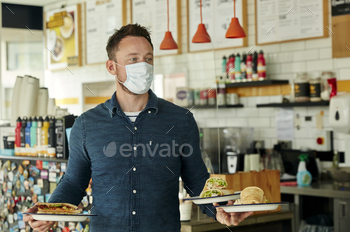 Waiter wearing mask holding two plates of food for customers