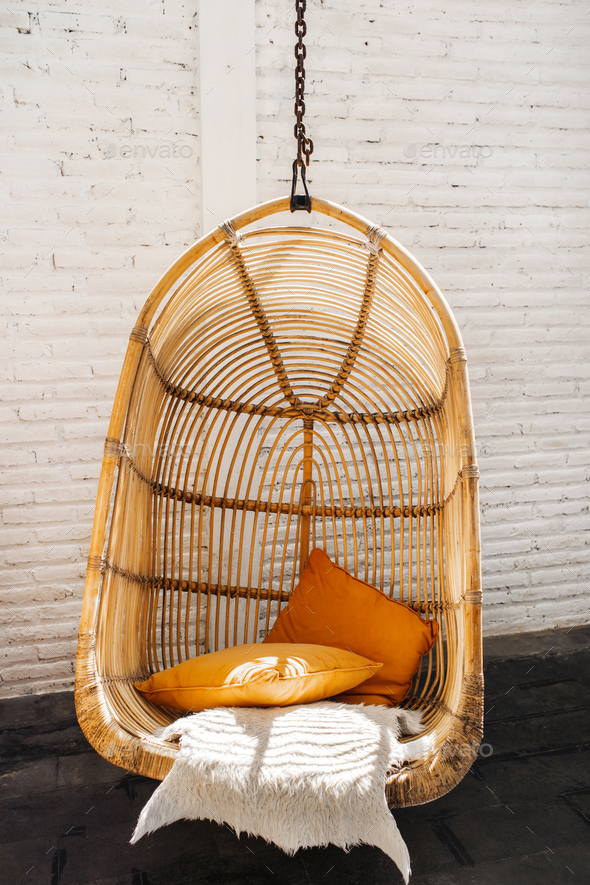 Wicker rattan hanging chair in loft cafe. Eco friendly furniture style and concept. Orange pillows