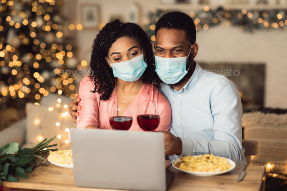 Black couple in masks using laptop, having virtual party