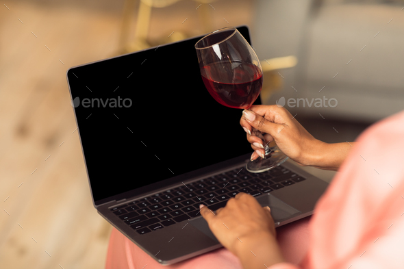 Black woman using laptop with empty mockup screen, drinking wine