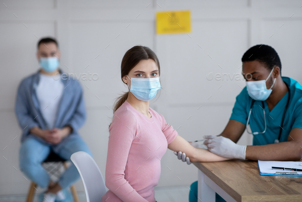 Black male doctor giving intramuscular injection to young woman at medical office