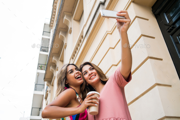 Two friends taking selfie with phone outdoors.