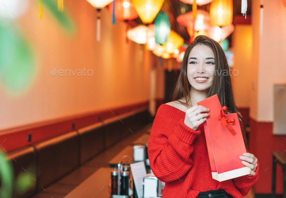 Asian woman in red clothes with red gift bag in restaurant celebrating Chinese New Year - Stock Photo - Images