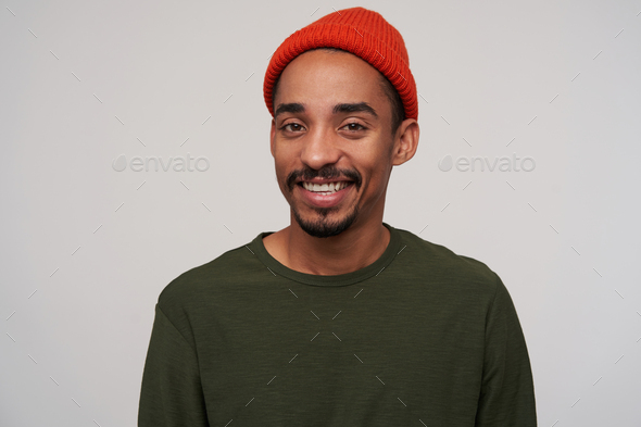 Portrait of beautiful young brown-eyed dark skinned male with beard looking cheerfully at camera - Stock Photo - Images