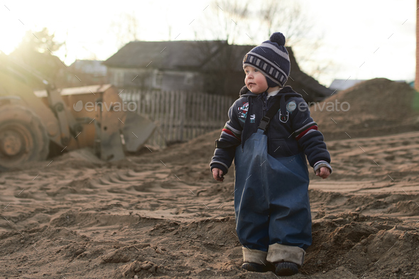 A boy in the village on the background of a tractor walks on the sand .