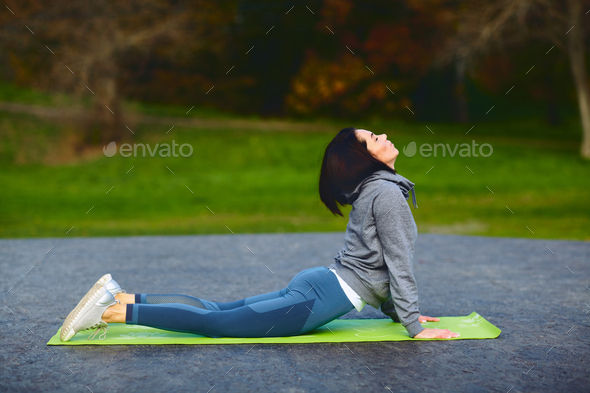 A brunette girl in a tracksuit performs morning sports exercises on yoga mat.