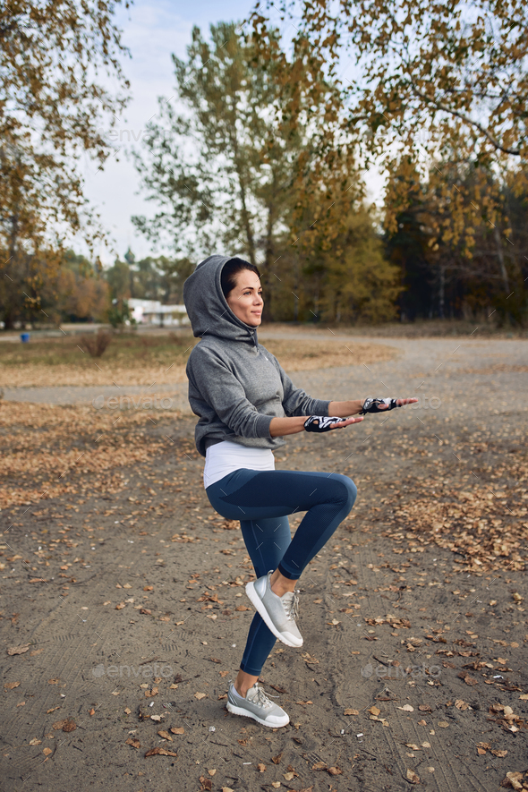 A brunette girl in a tracksuit performs morning sports exercises outside.