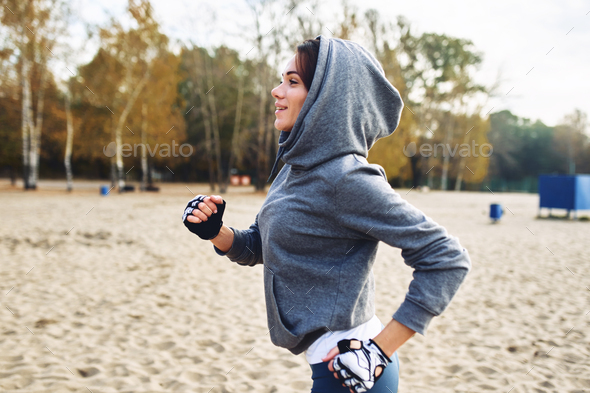 A brunette in a tracksuit runs on the street on the beach. Sports on the street.