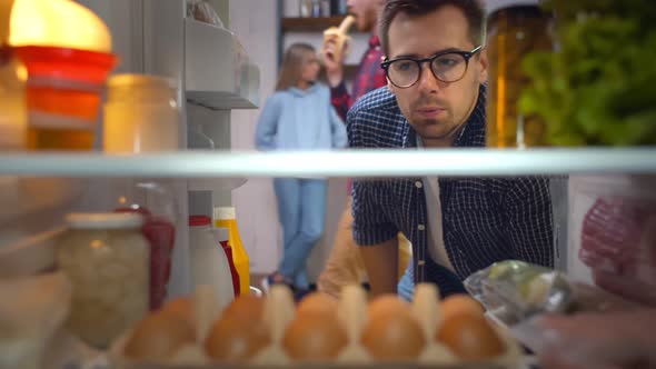 Young Guy Opening Fridge Looking for Snack Checking Time on Wristwatch and Grabbing Healthy Yogurt alt