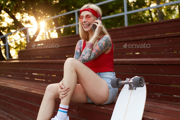 Young nice laughing blonde woman with tattooed arms, talking to his friend on smartphone
