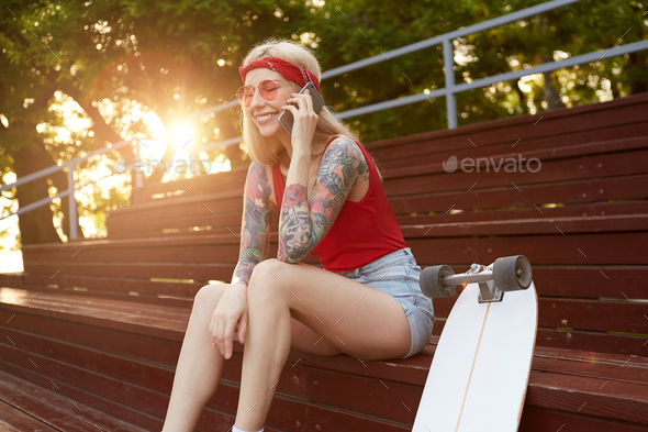 Young nice laughing blonde woman with tattooed arms, talking to his friend on smartphone