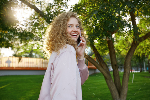 Outdoor photo of beautiful attractive charming curly hair young girl passes by, speaking