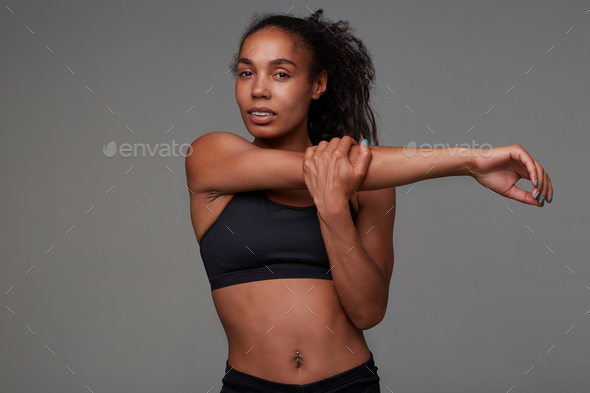 Attractive young dark skinned curly sportswoman with belly button piercing stretching