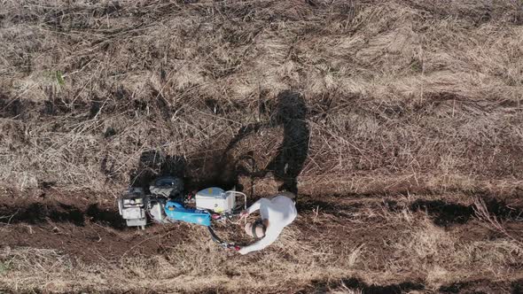 AERIAL - Man working a field with a rototiller, agriculture, wide shot zoom out alt