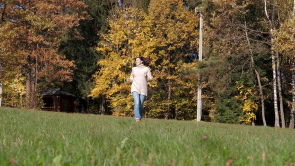 Happy Woman Joyfully Runs Across Green Lawn With Her Hands Raised To Side alt