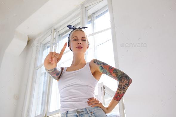 Indoor photo of young attractive tattooed lady dressed in casual clothes