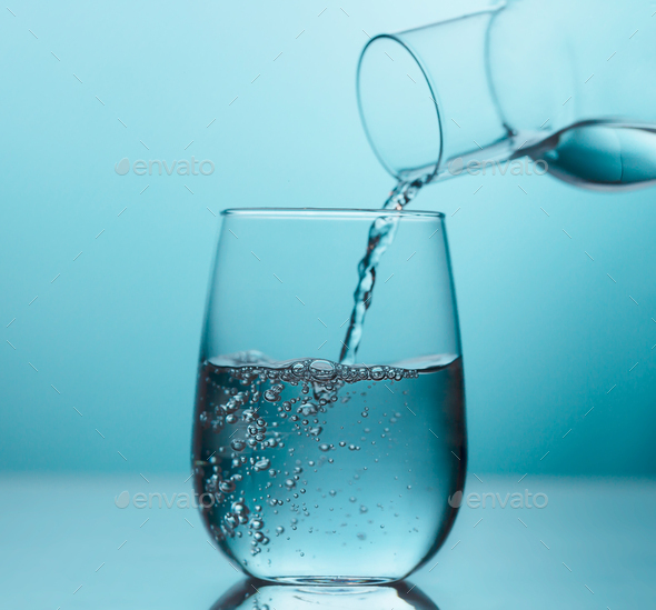 Fresh water pouring from the glass jug into a glass on the blue background  Stock Photo by Civil