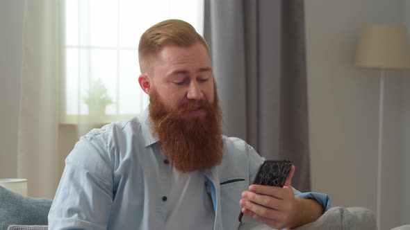 Happy Young Redhead Man Looking at Smartphone Screen Holding Web Camera Video Conversation with alt