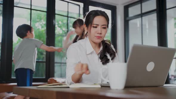 Asian business woman working at home due to COVID pandemic with their children playing around. alt