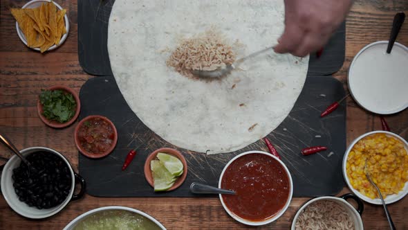 Overhead View of a Hand Preparing Tortilla By Adding Various Fresh Healthy Ingredients alt