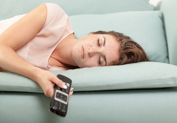 Young woman lying on couch and sleeping with TV remote control