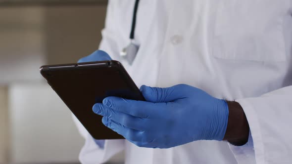 African american senior male doctor wearing white coat using digital tablet alt