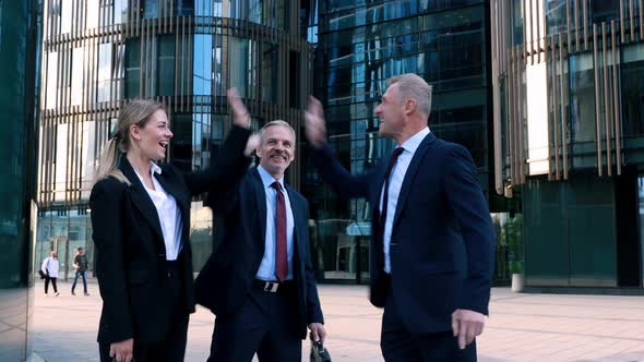 Two Businessmen and a Businesswoman in Suits Are Happy with Success and Give Each Other a High Five