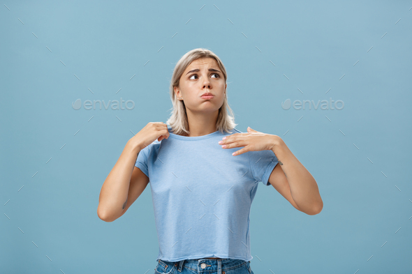 Girl feeling discomfort from heat standing over blue background in fug breathing out and frowning