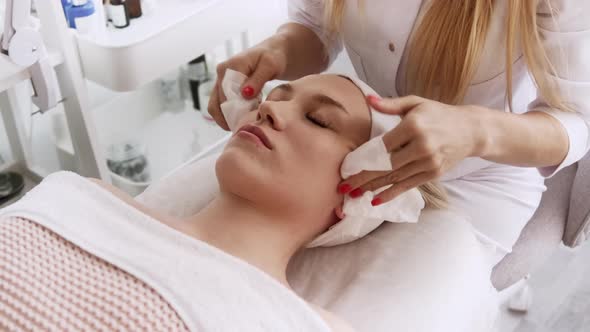 Beautician cosmetologist cleanses the skin of face before professional cosmetic procedure alt