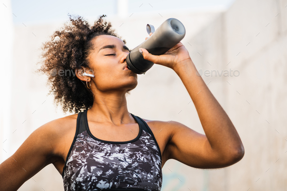 Afro athlete woman drinking water after work out outdoors.