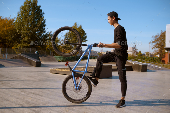 Male bmx biker doing trick, training in skatepark