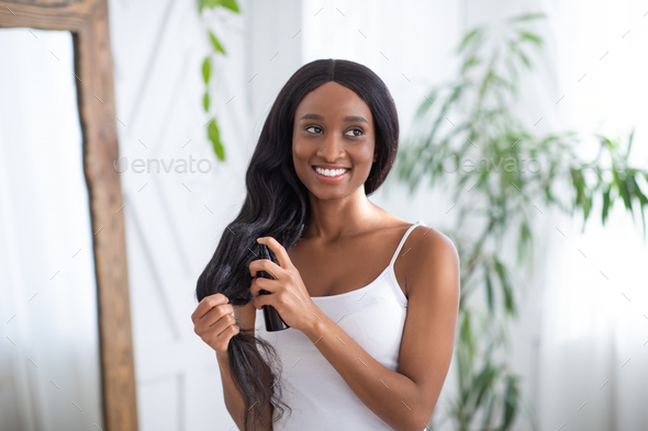 Hair care cosmetic. Happy millennial african american female apply hair care spray product on ends