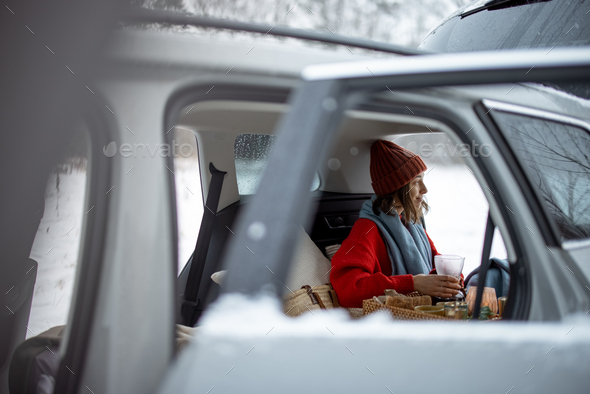 Woman have a coffee in car trunk in winter forest