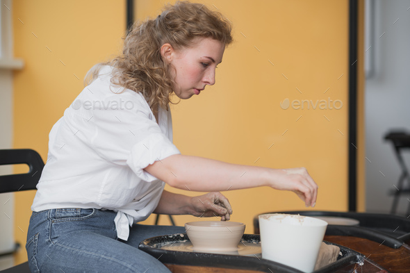 Woman working on potters wheel making dishes with their own hands. Close-up photo of dirty hands