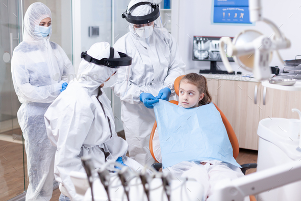 Little girl looking at dentist while assistant is putting her a bib
