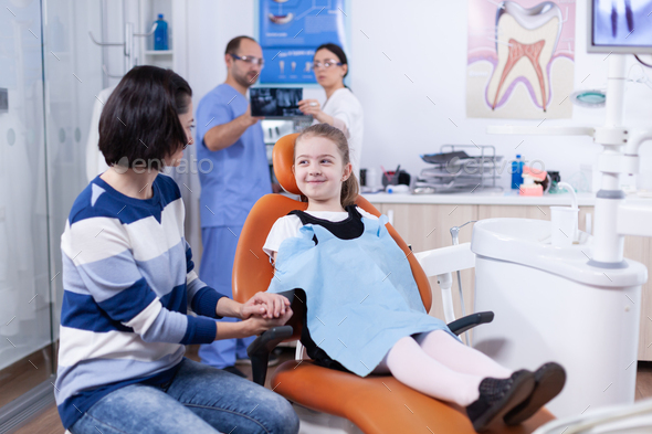 Happy little girl wearing dental bib in dentist office holding parent hand
