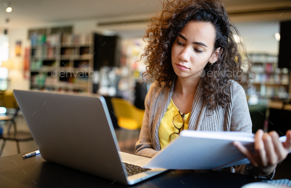Young afro american woman sitting at table with books and laptop for finding information