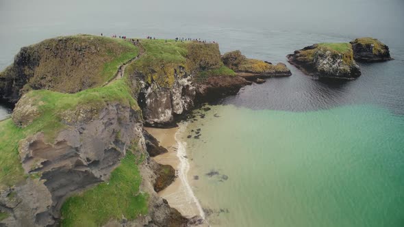 Ireland People Ocean Bay Aerial View: Tourists Walking on Carrick Islet, Carrick-a-Rede Rope Bridge alt