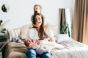 Cheerful mom with two children laughs and hugs and fools around on the bed in the bedroom.
