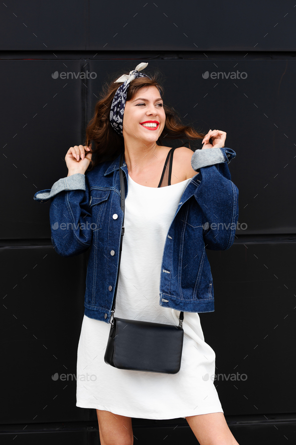 Gorgeous brunette girl with long flowing hair dressed in jeans jacket and jeans  poses standing on the dark background in the studio Stock Photo by  ©Leika_production 250033132