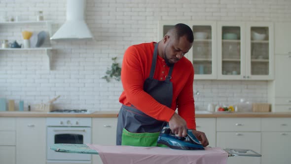 African Single Man Ironing Clothes with Steaming Iron alt