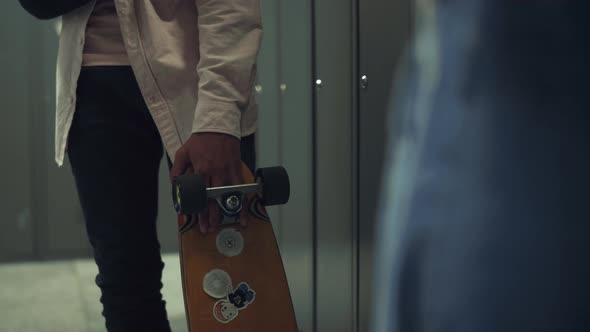 Boy Hand Holding Skateboard with Stickers in School Hall Close Up alt