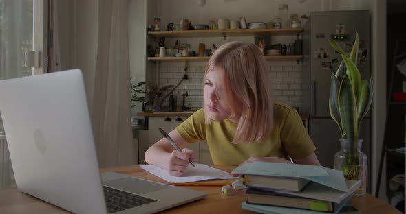 Adolescent Schoolgirl Studying Online Using Laptop Making Notes in Copybook alt