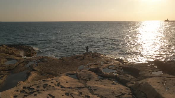Breathtaking aerial view of a fisherman fishing on flat rocks with the light of the setting sun refl alt