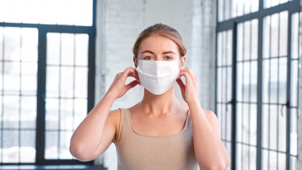 Happy young lady trainer in tracksuit takes off protective mask looking into camera alt