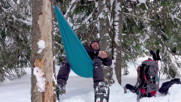 Hiker with snowshoes lying in hammock under the trees in the winter forest alt